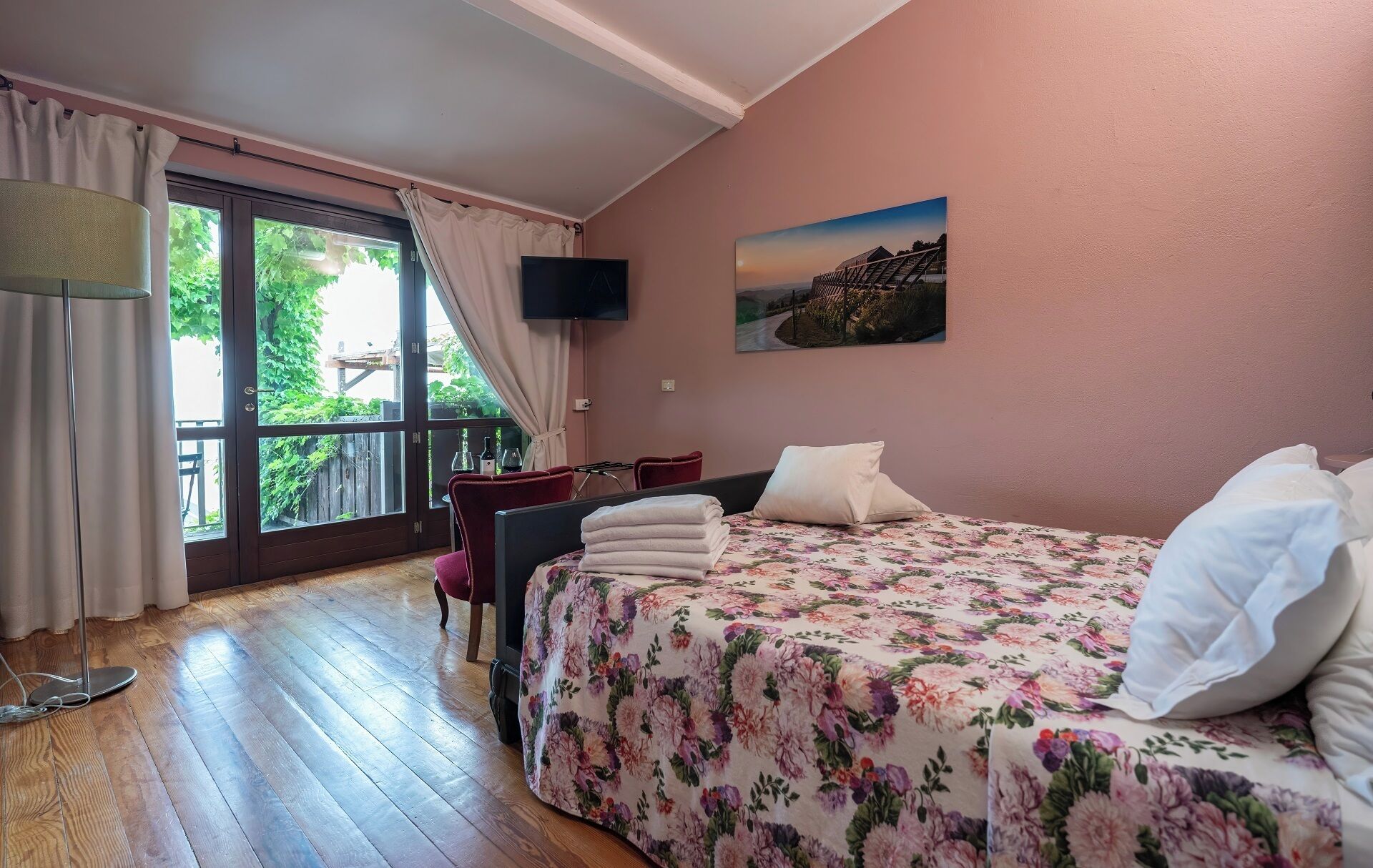 A bedroom with a bed, a TV, a window with curtains, and a painting on the wall.
