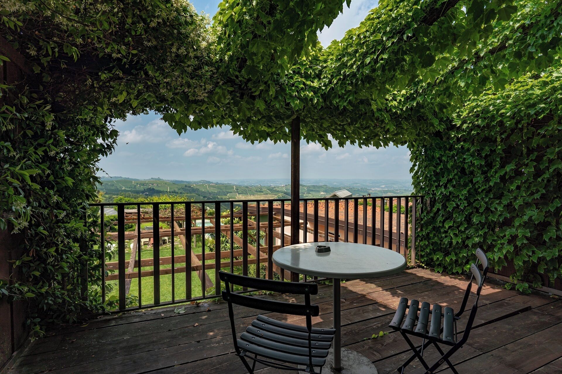 A patio with a round table and two chairs, surrounded by a wooden fence and lush greenery.