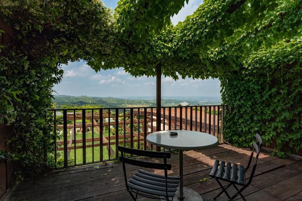 A patio with a round table and two chairs, surrounded by a wooden fence and lush greenery.