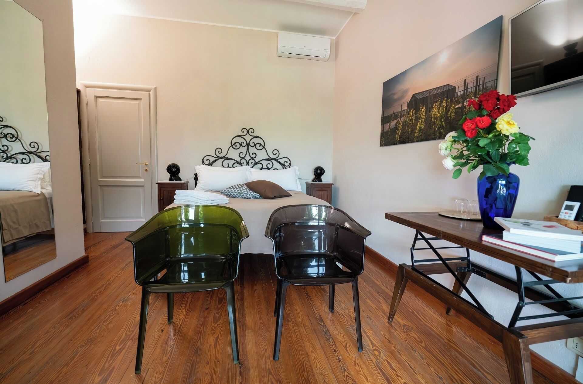 Un dormitorio con una cama, dos sillas, una mesa, un jarrón con flores y un cuadro en la pared.