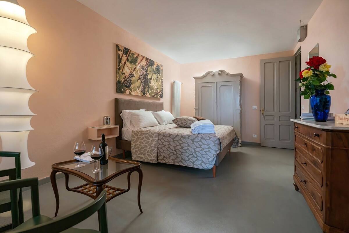Une chambre à coucher avec un lit, une table de chevet et une commode. Il y a une fenêtre avec des rideaux, une commode et un vase avec des fleurs.