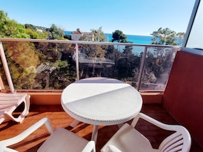 A balcony with a round table and white chairs, overlooking a coastal area with trees and buildings. - Sea view studio with Wi-Fi, 4 pax (Roquebrune-Cap-Martin)