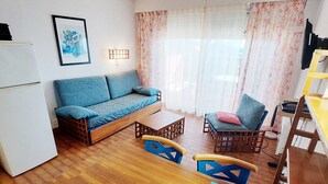 Un espace de vie compact comprenant un canapé, deux fauteuils, une petite table et un réfrigérateur.