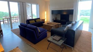 A spacious living room with a large sofa, a coffee table, and a fireplace. There is a view of the outdoors through large windows. - Alamo da Serra (Freixo)