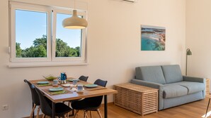 Ein modernes Wohnzimmer mit einem Holzesstisch, schwarzen Stühlen, einem grauen Sofa und einem großen Fenster mit Blick auf Bäume.