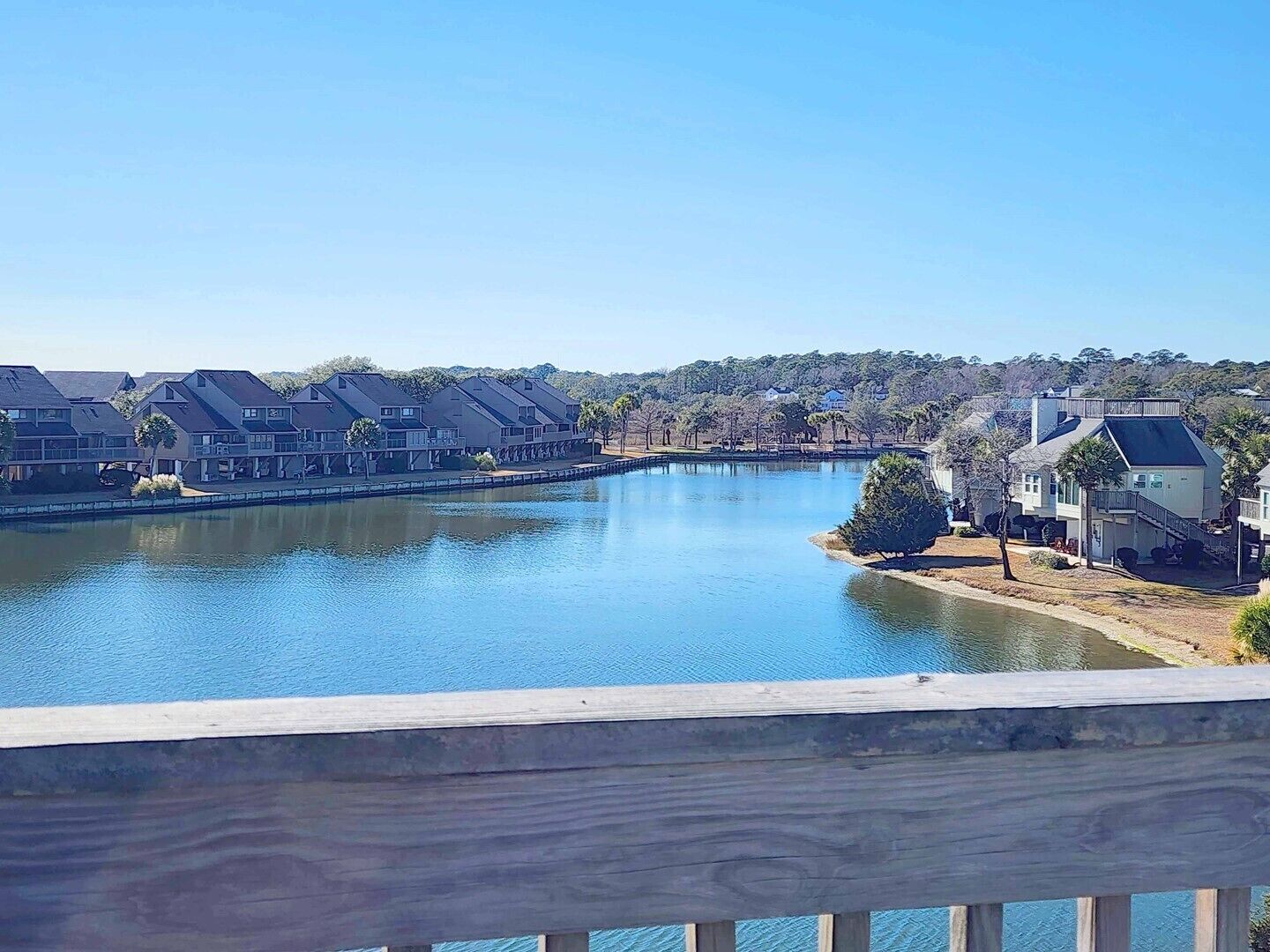 Un quartier résidentiel avec des maisons situées le long d’un plan d’eau paisible, probablement un lac ou une rivière, et une terrasse en bois au premier plan.