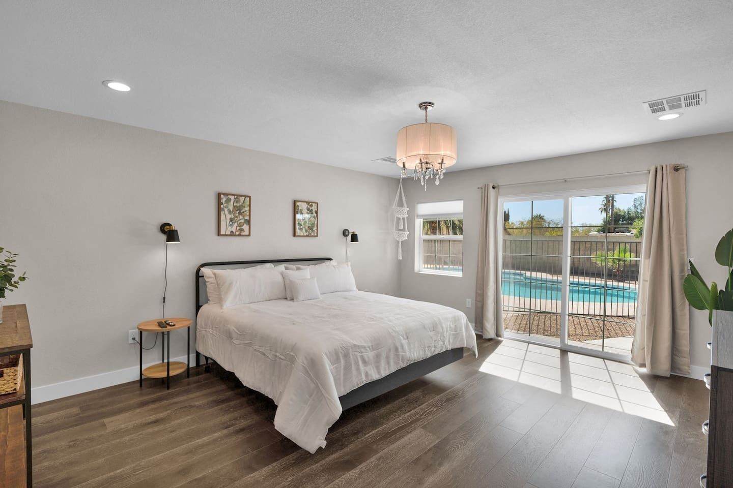A bedroom with a large bed, a nightstand, a lamp, and a view of a swimming pool through a sliding glass door.