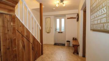 A hallway with a wooden staircase, a door with frosted glass panels, a small table with shoes, and a wall with motivational text.