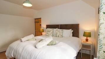 A neatly made bed with white linens and pillows, a wooden headboard, two bedside lamps, and a small bedside table.