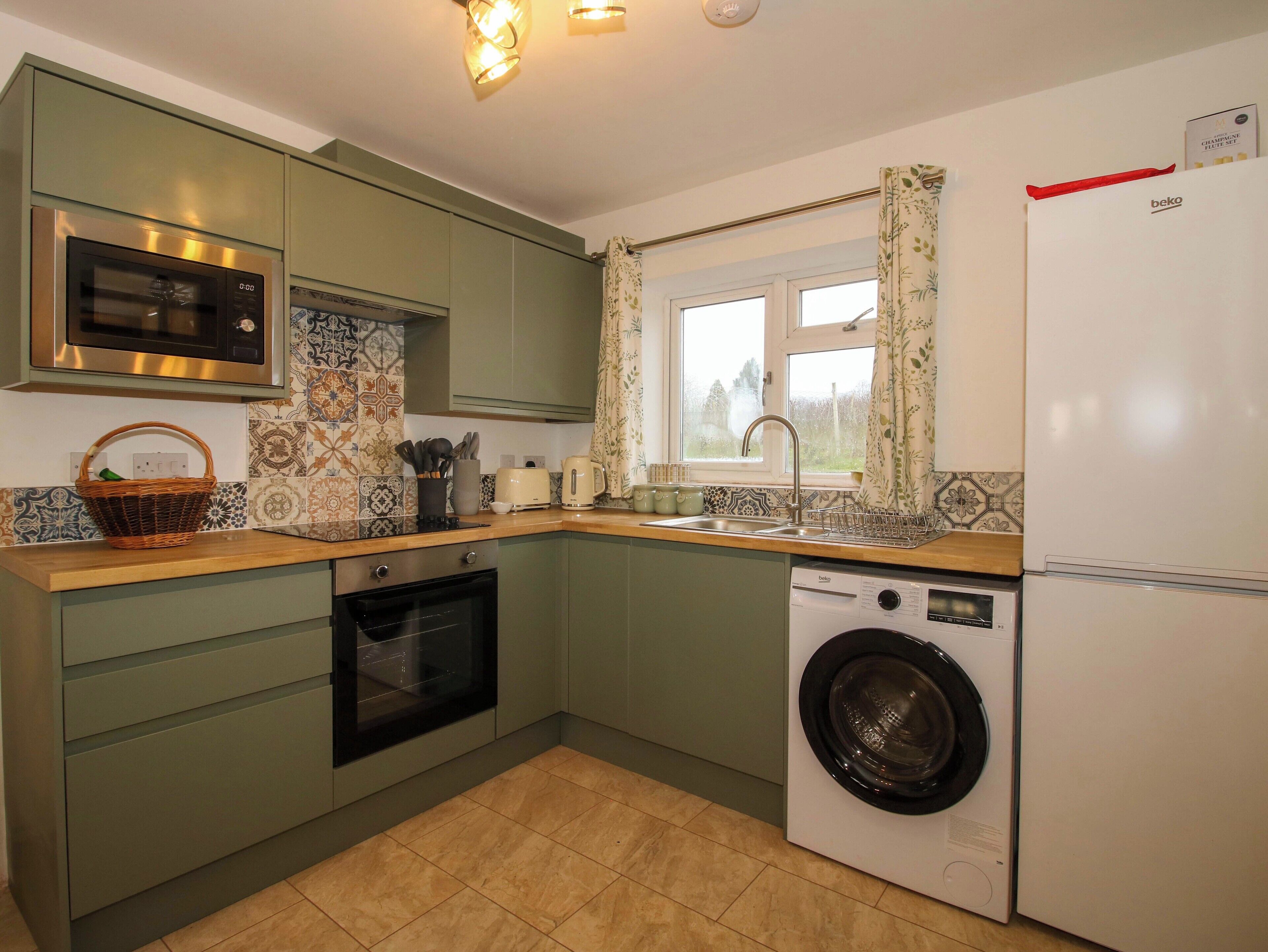 A compact kitchen with a microwave, oven, and washing machine, featuring green cabinets and patterned tiles.