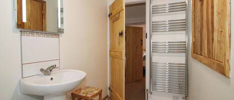 A bathroom with a white sink, a wooden stool, a mirror, and a wooden door leading to another room.