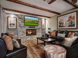 A living room with a stone fireplace, leather sofa, and a flat-screen TV mounted above it. - Sunny Backyard 5BR Minutes to Old Town Scottsdale (Scottsdale)