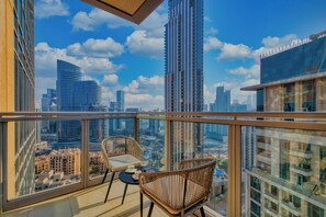 Ein Balkon mit Korbstühlen und einem kleinen Tisch, mit Blick auf eine Skyline moderner Gebäude und einem klaren Himmel.
