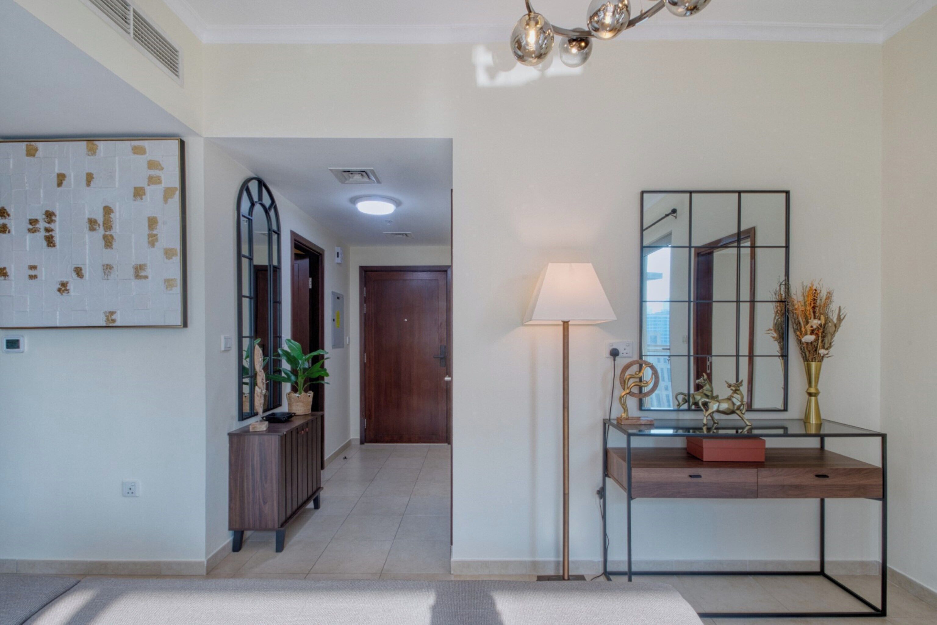A modern hallway with a wooden door, a console table with a lamp, and a mirror on the wall.