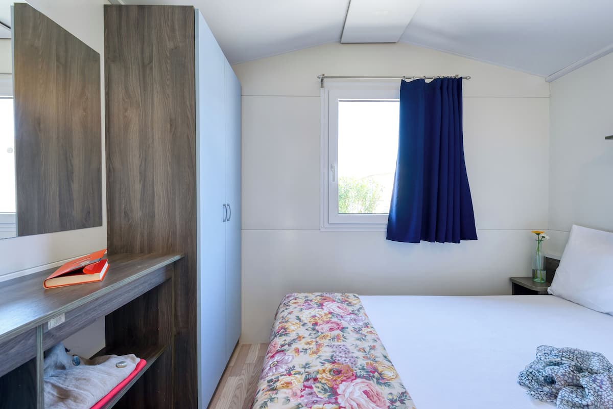A bedroom with a bed, a wardrobe, a window with curtains, a bedside table with a vase, and a nightstand.