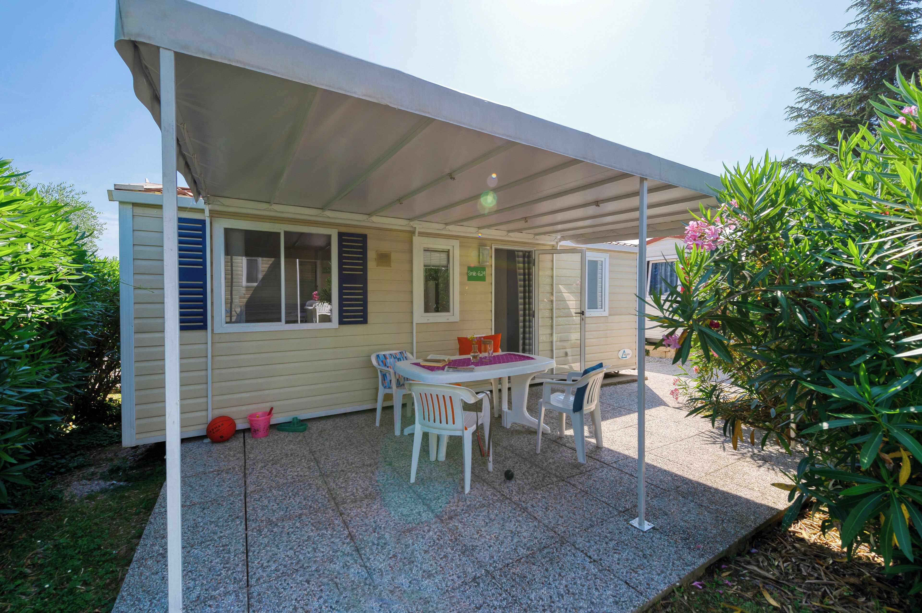 Un patio techado con una mesa y sillas, un jardín pequeño y un edificio de fachada color crema.