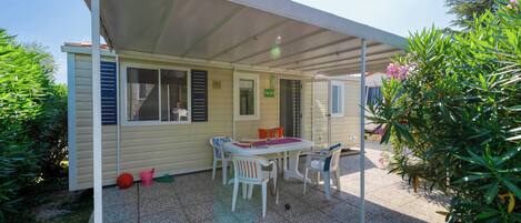Un patio techado con una mesa y sillas, un jardín pequeño y un edificio de fachada color crema.