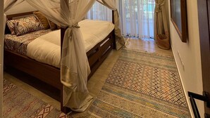 Ein Schlafzimmer mit Himmelbett, Deckenventilator und großem Fenster mit Vorhängen.