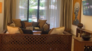Ein Wohnzimmer mit einer Couch, einem Couchtisch und einem Laptop. Ein Fenster mit Vorhängen, ein Bild an der Wand und ein Holzboden.