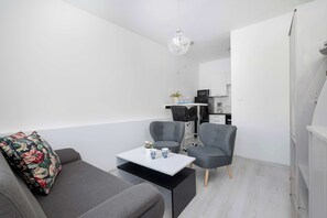 Ein modernes Wohnzimmer mit grauem Sofa, zwei Sesseln, einem weißen Couchtisch und einer Küchenzeile im Hintergrund.