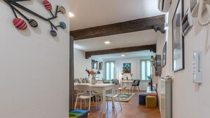Een ruime woonkamer met een eettafel, stoelen en een bank. Er is een radiator aan de muur en een trap die naar een ander niveau leidt.