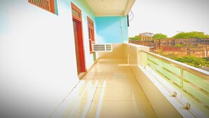 Un balcone con pavimento piastrellato, una finestra con inferriate e vista su edifici sullo sfondo.