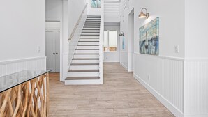 A spacious hallway with a wooden floor, white walls, and a staircase leading to another level. - 6BR Gulf-Front w/ Private Beach & Pool (Panama City Beach)