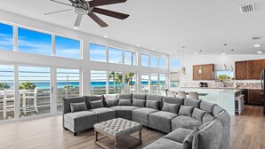 A spacious living area with a large gray sectional sofa, a wooden ottoman, and a view of the ocean through large windows. - 6BR Gulf-Front w/ Private Beach & Pool (Panama City Beach)