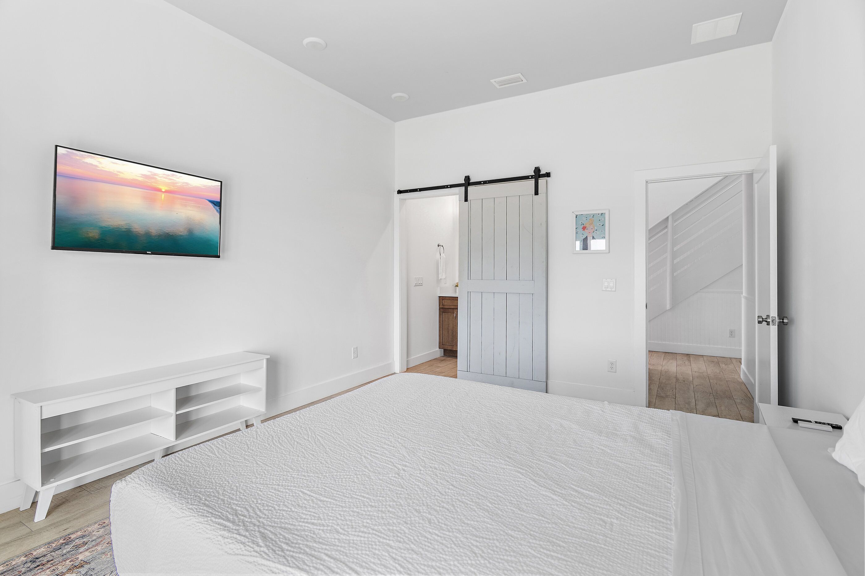 A bedroom with a large bed, a mounted TV, a sliding door, and a white console unit.