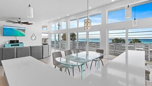 A modern dining area with a glass table and chairs, a ceiling fan, and large windows overlooking the ocean. - 6BR Gulf-Front w/ Private Beach & Pool (Panama City Beach)