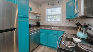 Une cuisine compacte avec des meubles de couleur turquoise, un réfrigérateur en acier inoxydable, une cuisinière à gaz et un four à micro-ondes.