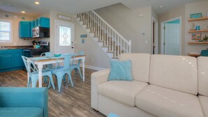 Un vaste espace de vie comprenant un canapé beige, une table à manger avec des chaises, une cuisine aux armoires de couleur turquoise et un escalier.