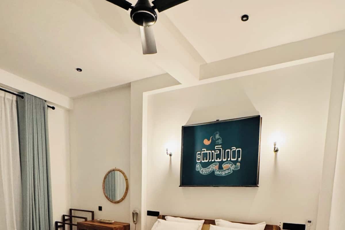 A bedroom with a bed, a ceiling fan, a wall-mounted TV, a bedside table, and a nightstand.