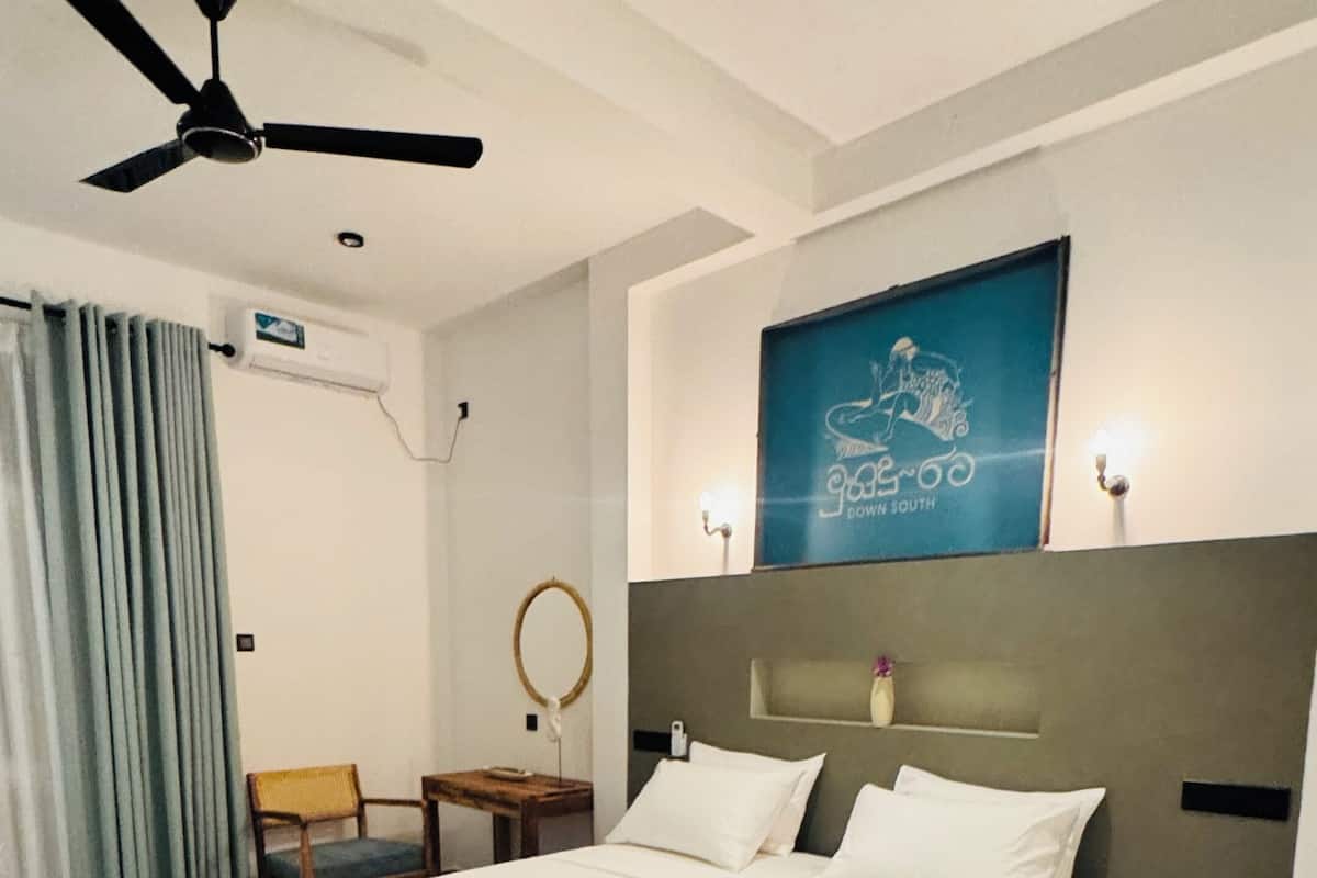 A modern bedroom with a large bed, a ceiling fan, a wall-mounted air conditioner, and a framed artwork.
