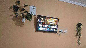 Une pièce avec un téléviseur à écran plat fixé au mur, un haut-parleur noir, un clavier et un jeu de cartes posé sur le sol.