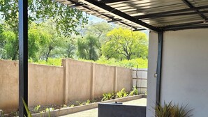 Un espace extérieur abrité, doté d’un sol en béton, de bancs en métal et de plantes en pot.