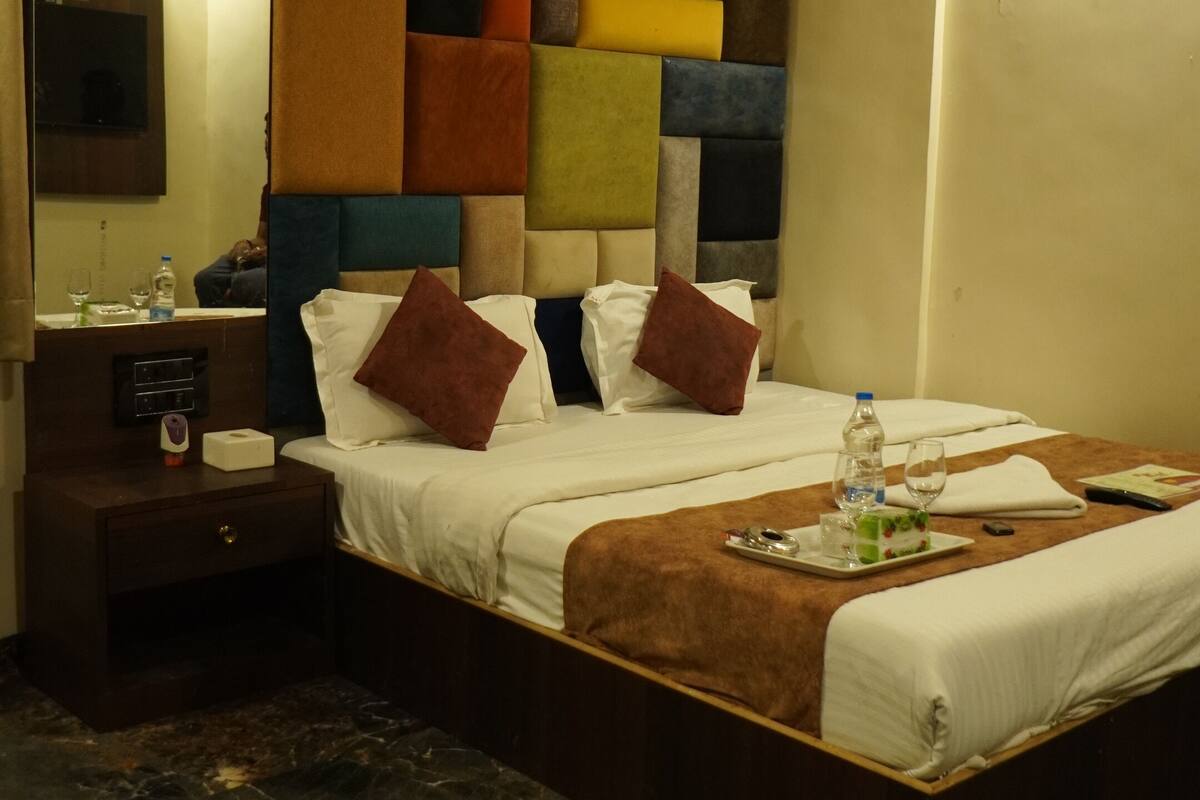 Ein Hotelzimmer mit Bett, Nachttisch, Spiegel und einem Kopfteil mit farbigem Muster.