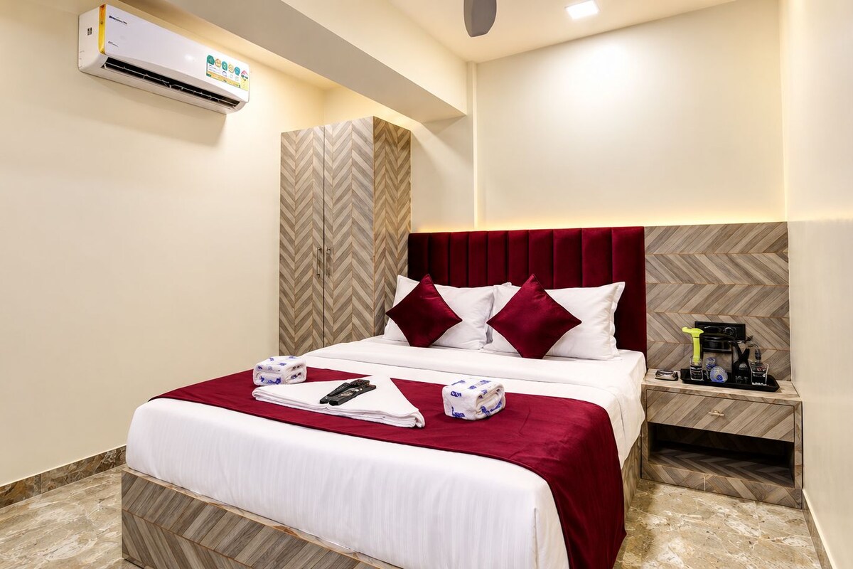 A hotel room with a bed, a bedside table, an air conditioning unit, and a herringbone-patterned wall.