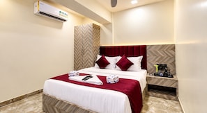 A hotel room with a bed, a bedside table, an air conditioning unit, and a herringbone-patterned wall. - Hotel Versova Inn (Mumbai)