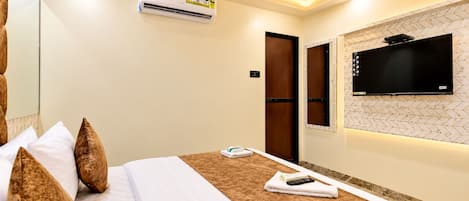 A hotel room with a bed, pillows, a remote control, a TV, and an air conditioning unit.