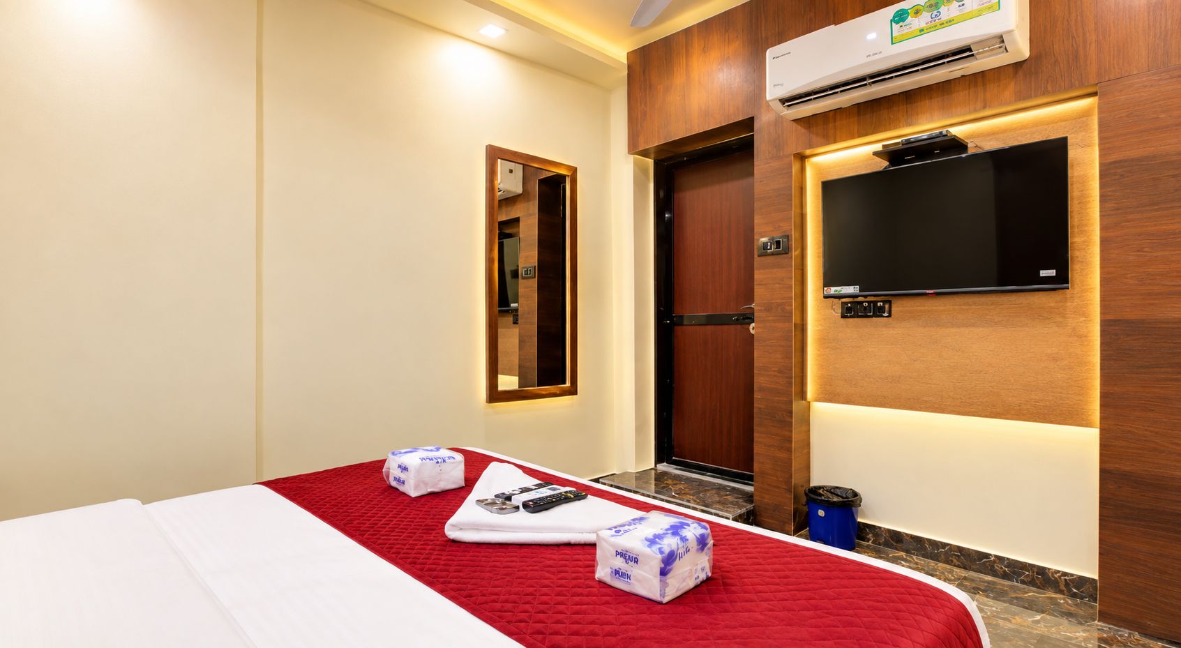 A hotel room with a bed, a TV mounted on the wall, and a wooden door.