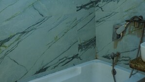 A bathroom with a marble wall, a bathtub, and a shower area. - Hotel Versova Inn (Mumbai)