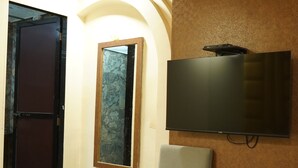 A hotel room with a TV mounted on the wall, a chair, a table with a red table runner, and a window with a view of a building. - Hotel Versova Inn (Mumbai)
