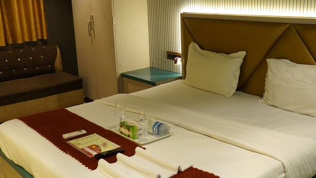 A hotel room with a large bed, a bedside table, a nightstand, a wardrobe, and a ceiling fan. - Hotel Versova Inn (Mumbai)