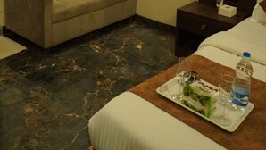 A hotel room with a sofa, a small table with a tray of food and drinks, a bed, a nightstand, a mirror, and an air conditioning unit. - Hotel Versova Inn (Mumbai)