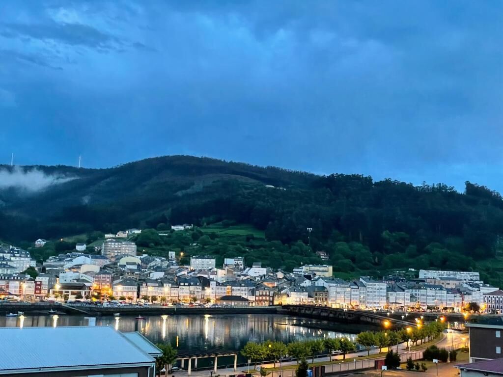 Un paisaje urbano costero con un río, edificios y una colina al fondo.