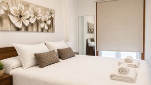 A hotel room with a large bed, a wall-mounted artwork of flowers, a mirror, and a window with a blind. - APARTMENT WITH SEA VIEW (Viveiro)