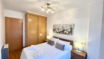 A bedroom with a bed, wooden wardrobe, and a wall-mounted artwork.