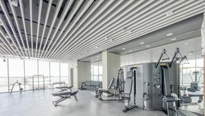 Ein modernes Fitnessstudio mit verschiedenen Trainingsgeräten, großen Fenstern und einer hohen Decke mit linearer Beleuchtung.
