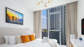 Una habitación de hotel moderna con una cama grande, un cuadro de un paisaje urbano, una ventana con cortinas y un televisor de pared mostrando el logo de Netflix.